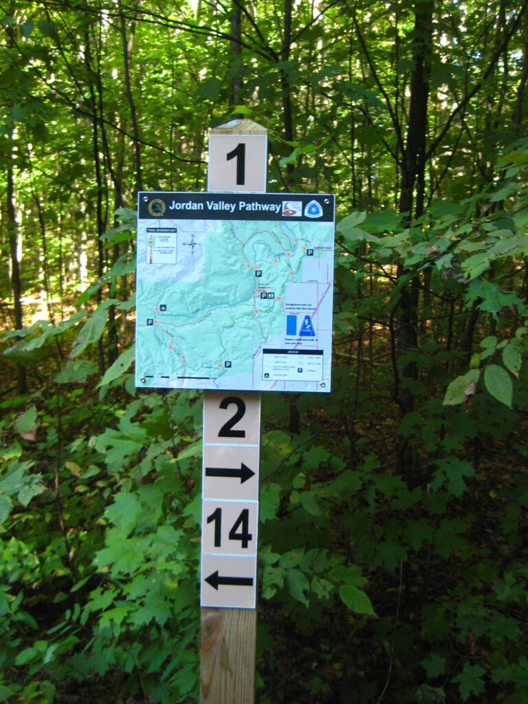 A trail marker with a map the number one above the map and the number two below the map with an arrow pointing right, and the number 14 with an arrow pointing left.