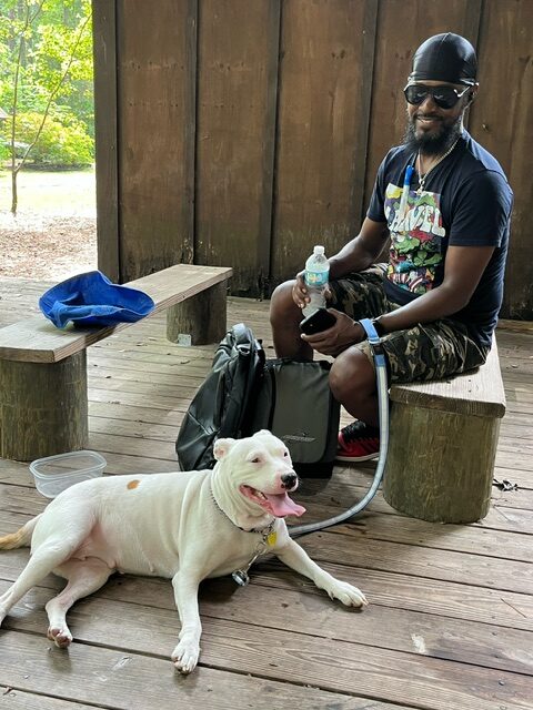 A man is sitting on a bench resting with his dog lying on the floor.